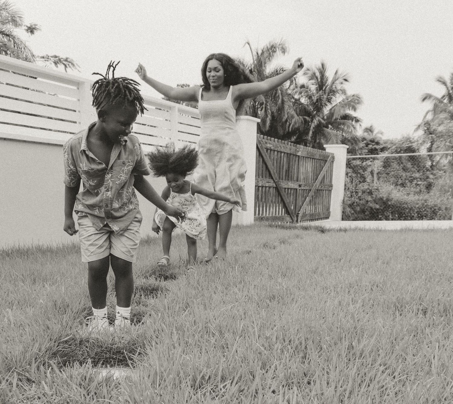 Joyful outdoor playtime as people jump and play in a grassy backyard with palm trees in the background.