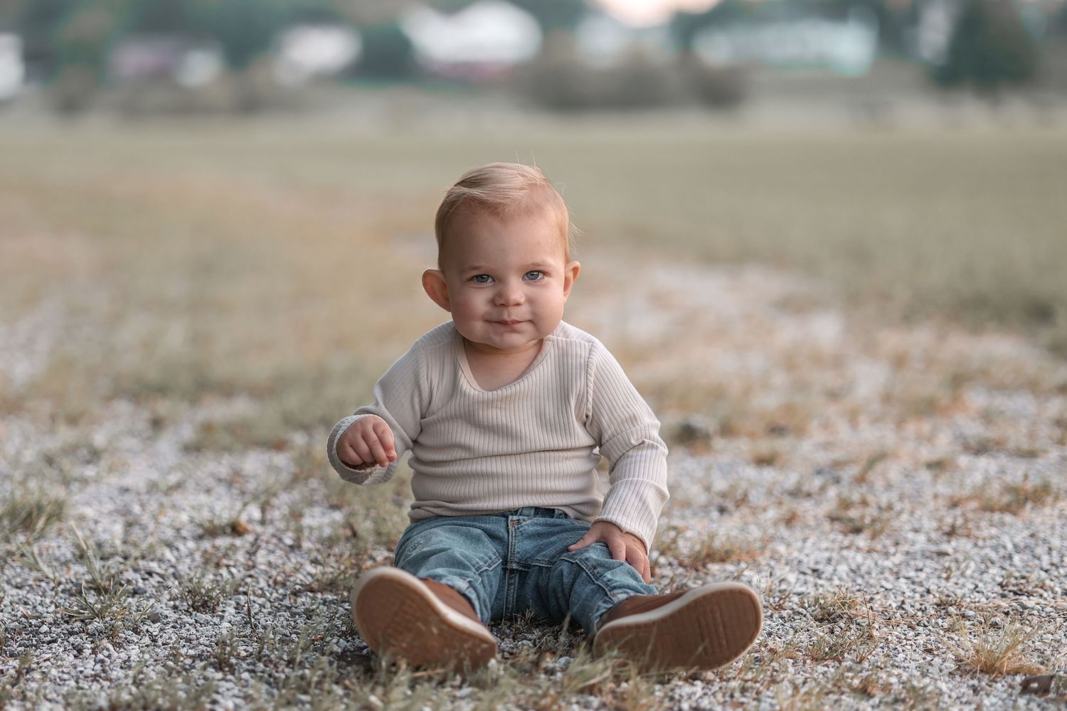 A small child in a cream sweater sits on frosty ground with a happy expression.