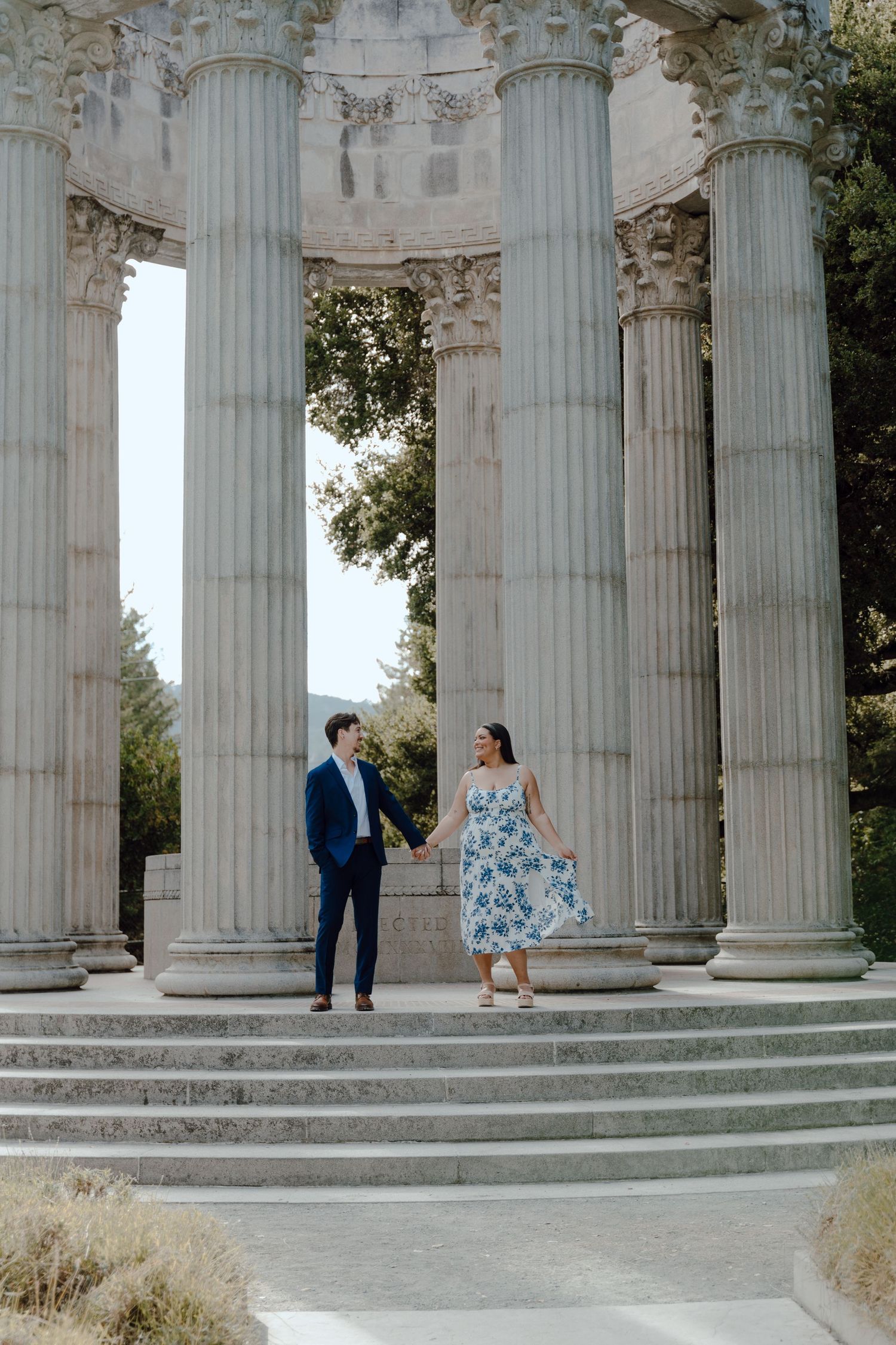 A couple poses between grand classical columns at a historic monument site.