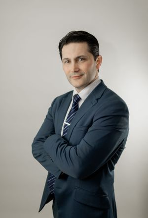 Professional portrait of a person in a dark business suit against a light backdrop.