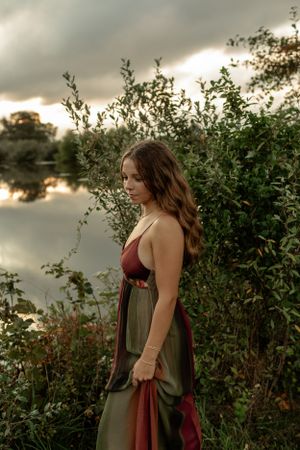Moody lakeside portrait in a burgundy and olive dress during sunset.