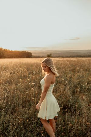 Figure in flowing white dress standing in wildflower meadow at sunset.