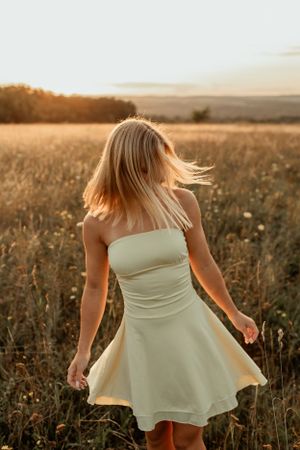 Person twirling in white summer dress in golden field at dusk.