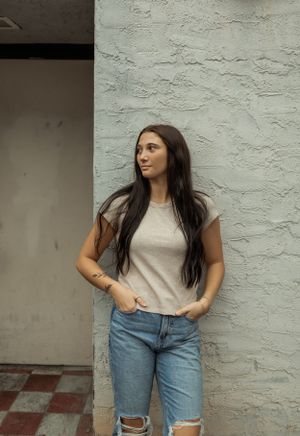 Casual style portrait against textured grey wall featuring ripped jeans and neutral t-shirt.
