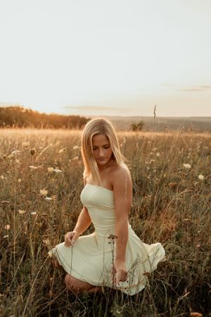 Figure in cream colored dress posing in meadow during sunset.