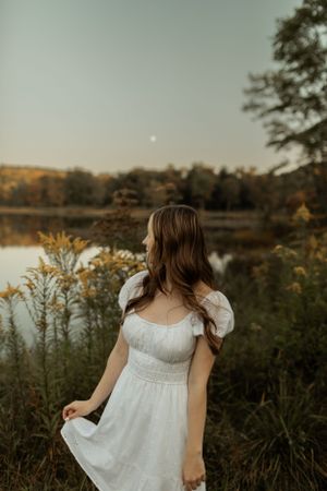White dress silhouette against sunset lake with autumn foliage in background.