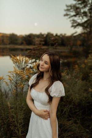 Romantic portrait in white dress by lakeside during golden hour.