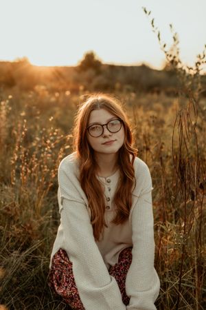 Warm sunset portrait in cozy sweater amidst tall dried grasses.