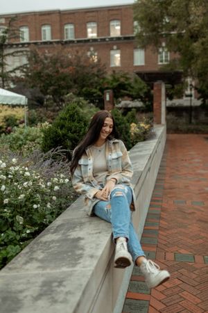 Relaxed outdoor portrait on brick wall ledge near flowering garden and historic building.