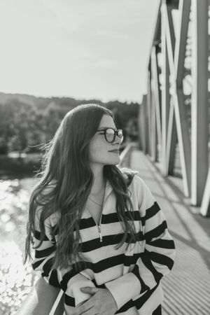Black and white portrait on bridge with striped sweater and glasses.