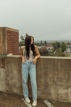 Person in casual attire poses against brick wall on rooftop overlooking misty cityscape.