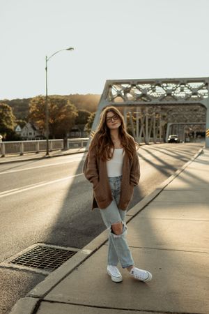 Casual autumn street style pose on metal bridge at golden hour.