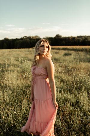 Golden hour portrait in flowing pink maxi dress standing in wild meadow.