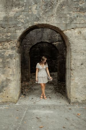 Artistic photo of someone in a floral dress standing in a stone archway.