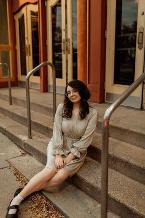 Person sitting on concrete steps wearing beige dress outside historic building.
