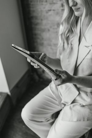 Blonde woman in white suit holding a tablet device, black and white professional photo.