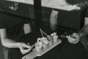 Black and white photo of two people sharing desserts on a wooden board with spoons.