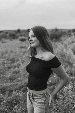 Black and white portrait of a woman in casual attire smiling while posing outdoors in a natural setting.