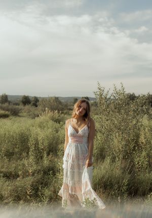 A dreamy outdoor portrait of someone in a flowing white lace dress standing among wild grasses at golden hour.