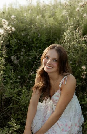 Carefree person in white floral dress sitting outdoors enjoying a sunny summer day among green foliage.