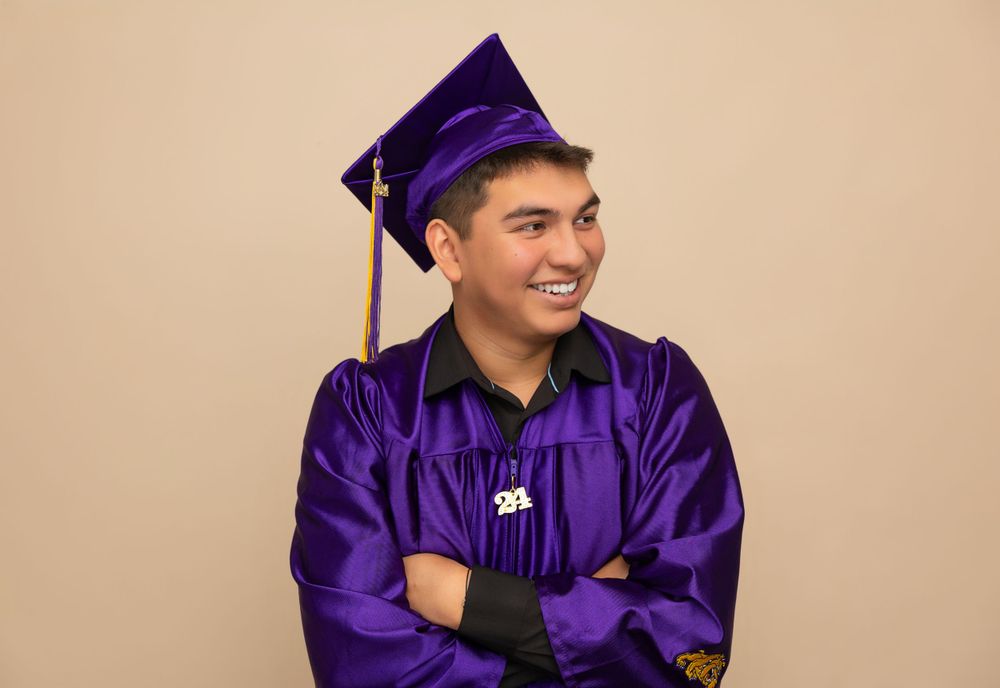 Graduate in purple regalia poses with crossed arms and bright smile.
