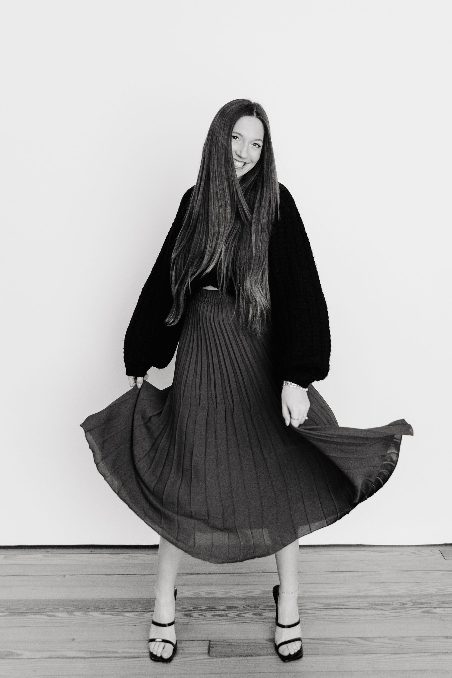 Young woman in black pleated midi skirt and jacket twirling in black and white fashion portrait.