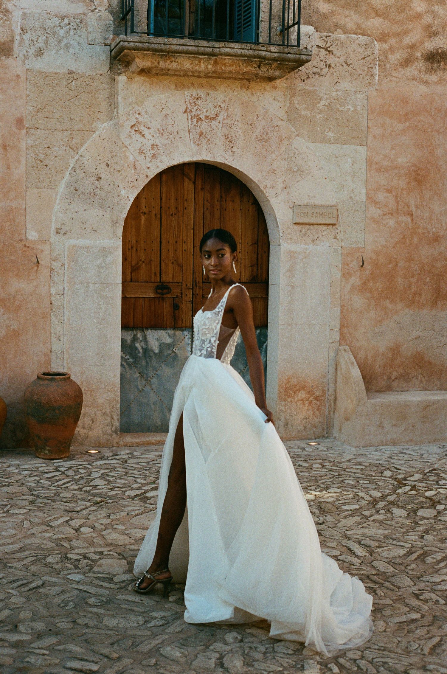 A stunning wedding gown with a dramatic slit photographed against a Mediterranean stone facade.