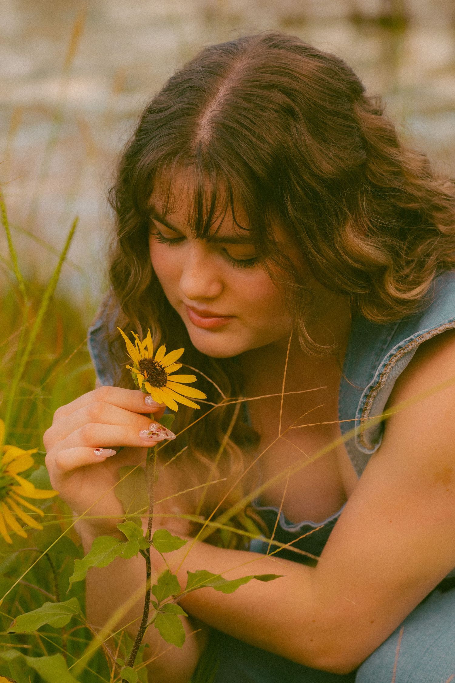 Person smelling a bright yellow sunflower in a dreamy outdoor setting.