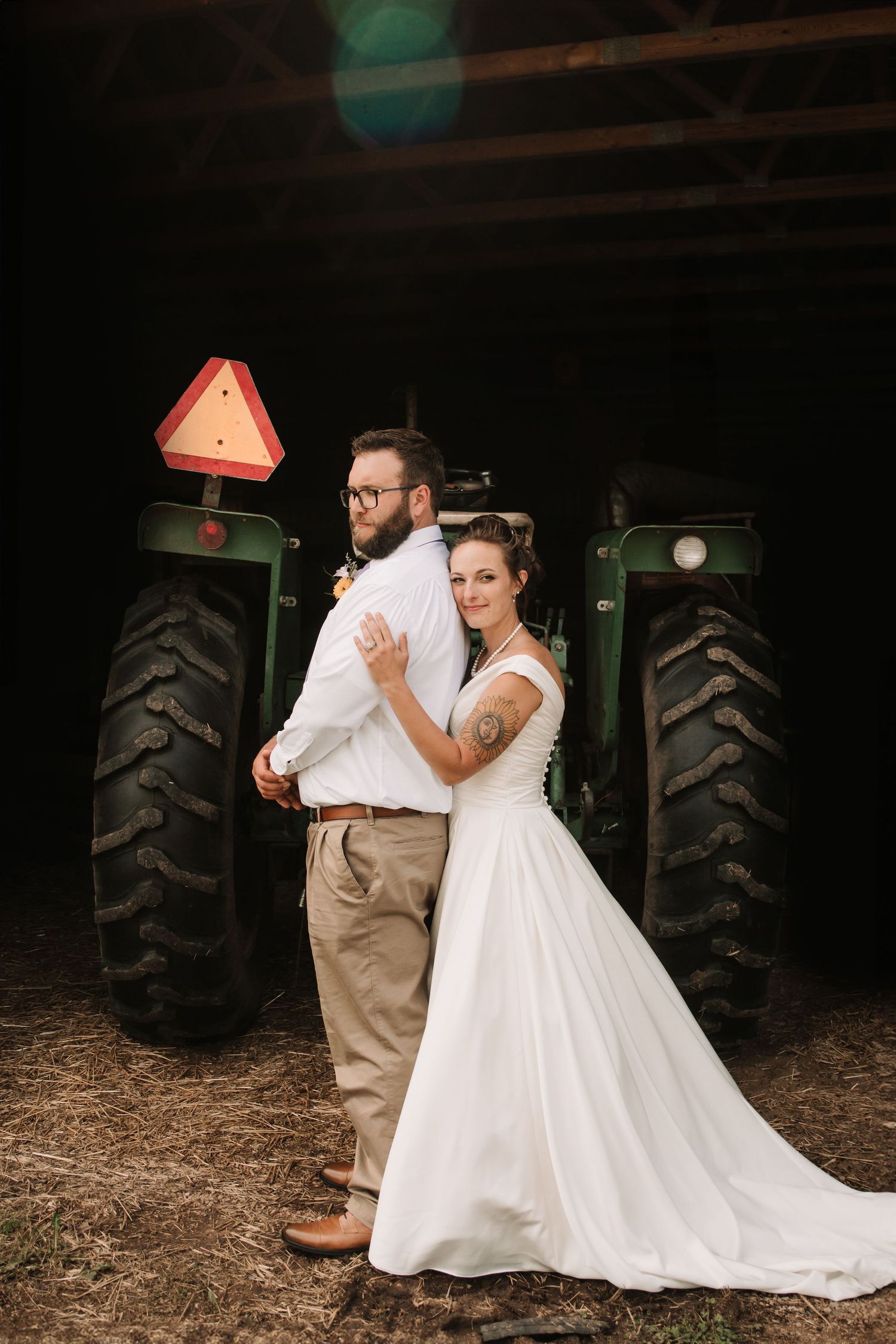 Wedding couple poses in front of green tractor in rustic farm setting.