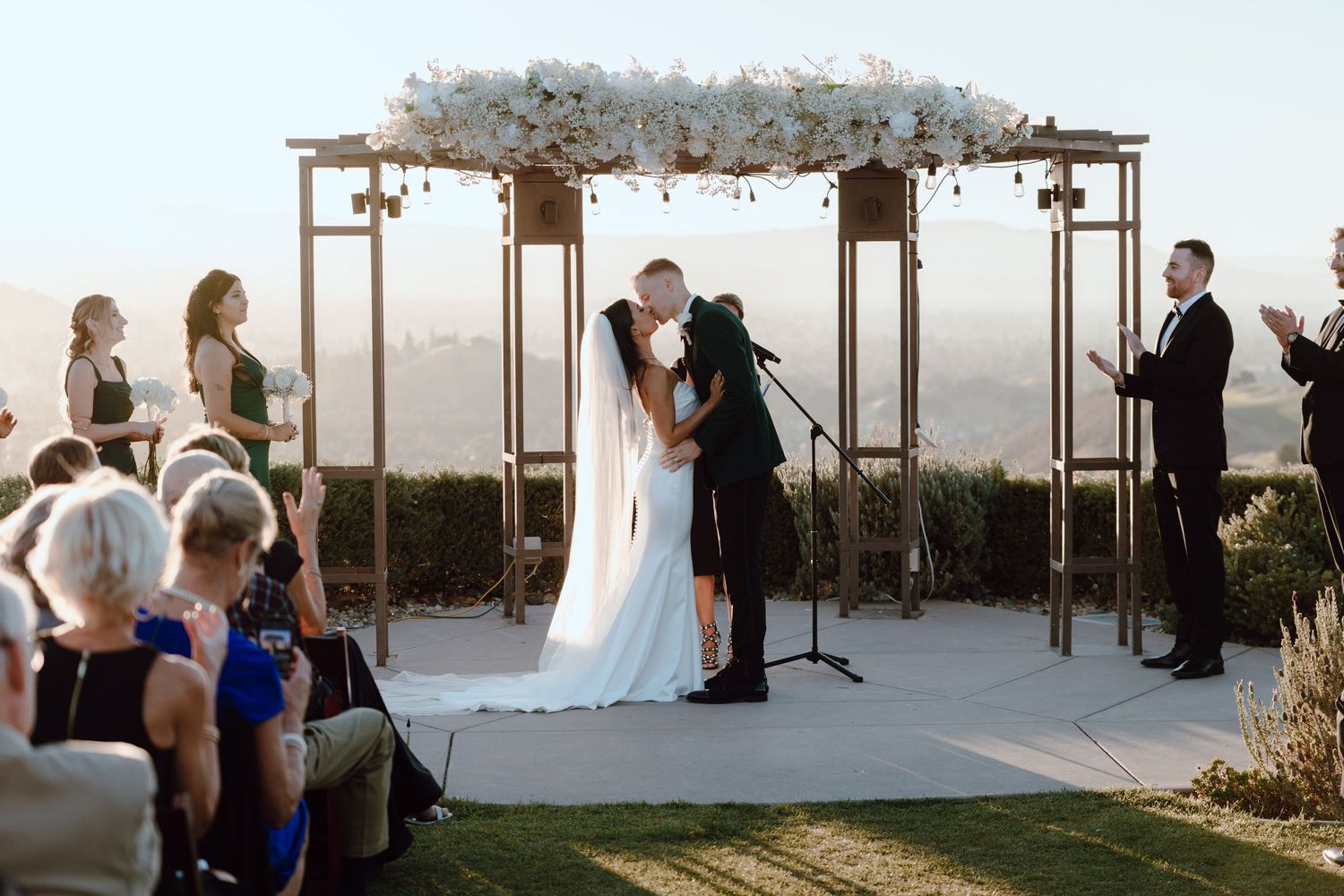 An intimate wedding ceremony under a floral arch with guests seated outdoors.