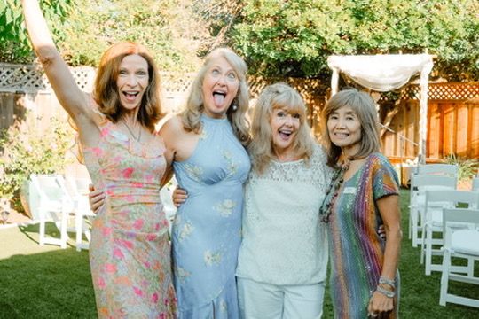A joyful group of friends sharing laughter and embracing during a special gathering outdoors on a sunny day.