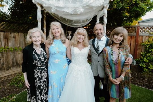 Wedding party posed outdoors wearing light blue bridesmaid dresses and formal attire in a backyard garden setting.