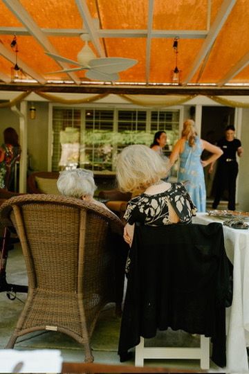 On an orange-ceilinged patio, people gather at a table with wicker chairs during what appears to be a social event.