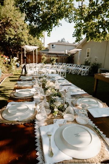 A long elegant outdoor table setting with white plates and glassware arranged on a white tablecloth for a garden party.