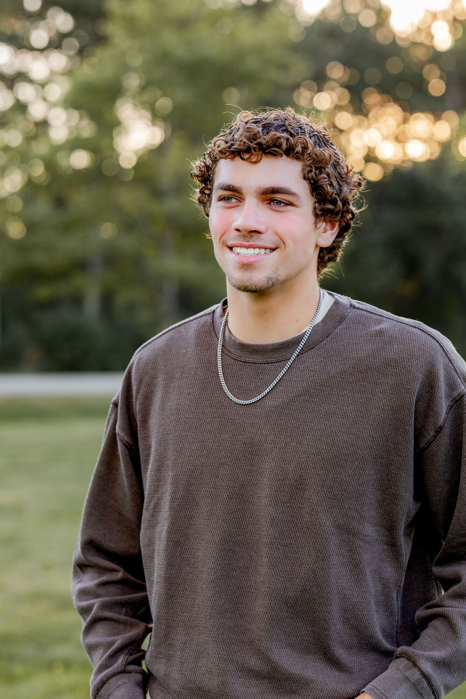 Soccer player in ripped jeans sits on path with ball near stone bridge.