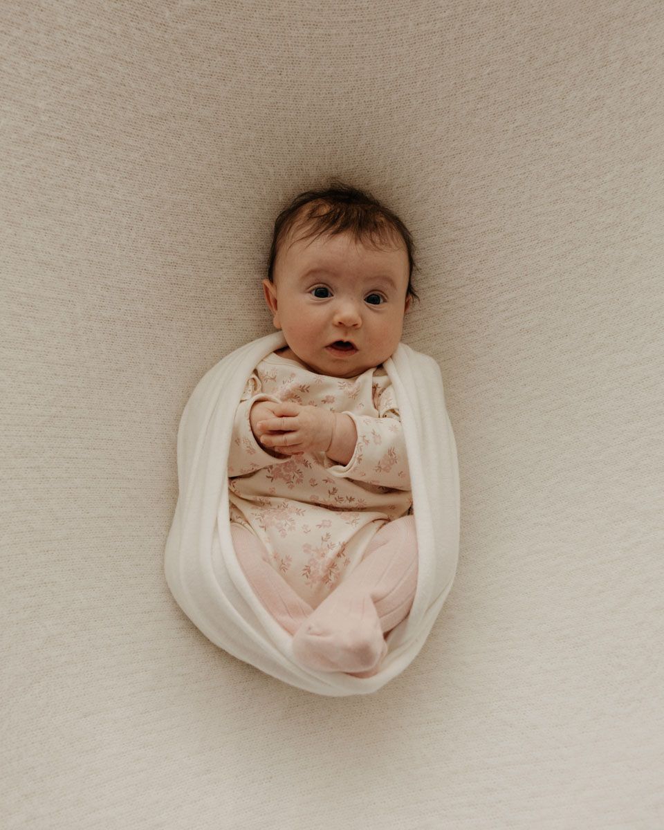 Creative overhead shots of baby wrapped in white fabric against textured background.