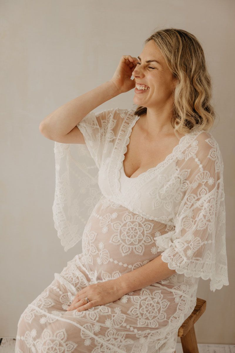 Light and airy maternity portraits with woman in delicate white lace dress.