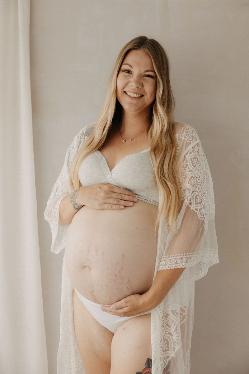 Maternity boudoir photos featuring white lace robe against neutral backdrop.