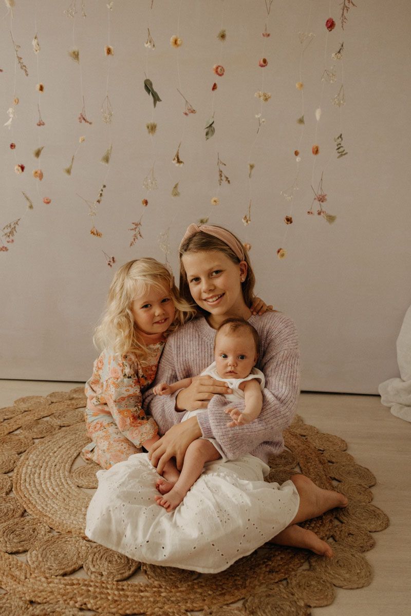 A sweet family portrait with children sitting on a round jute rug against a neutral backdrop.