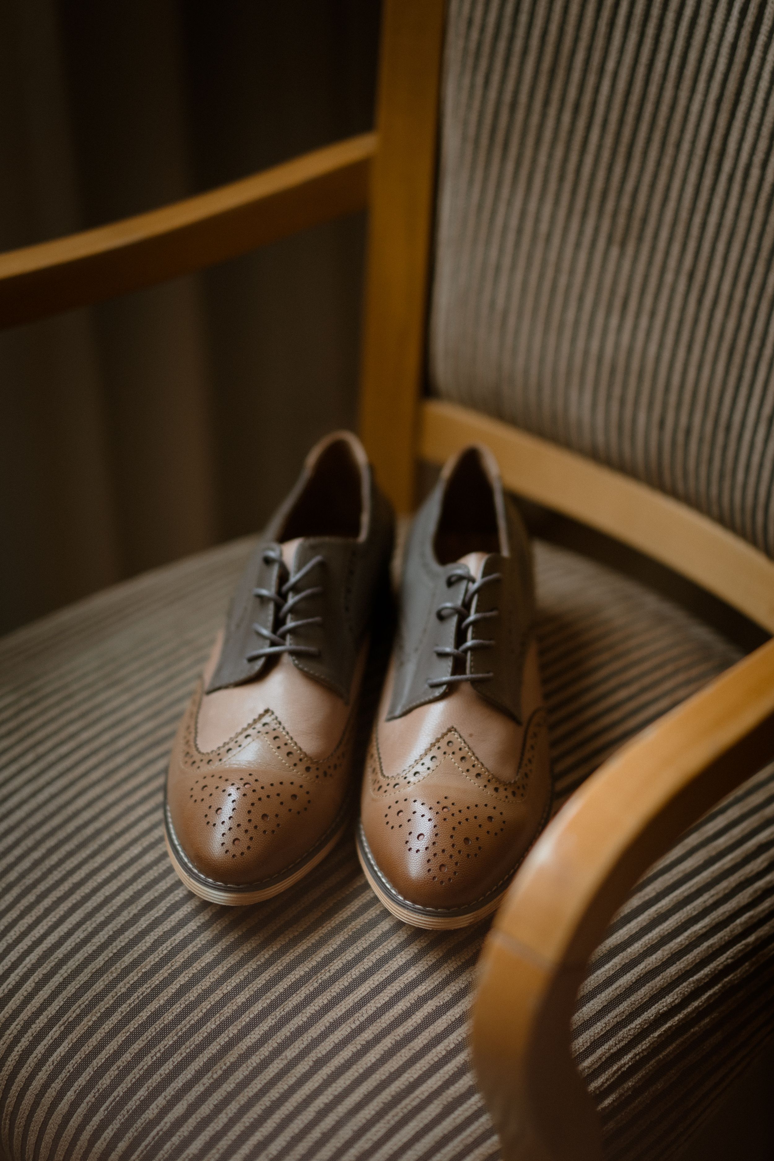 Brown leather oxford dress shoes with brogue detailing placed on striped upholstery.