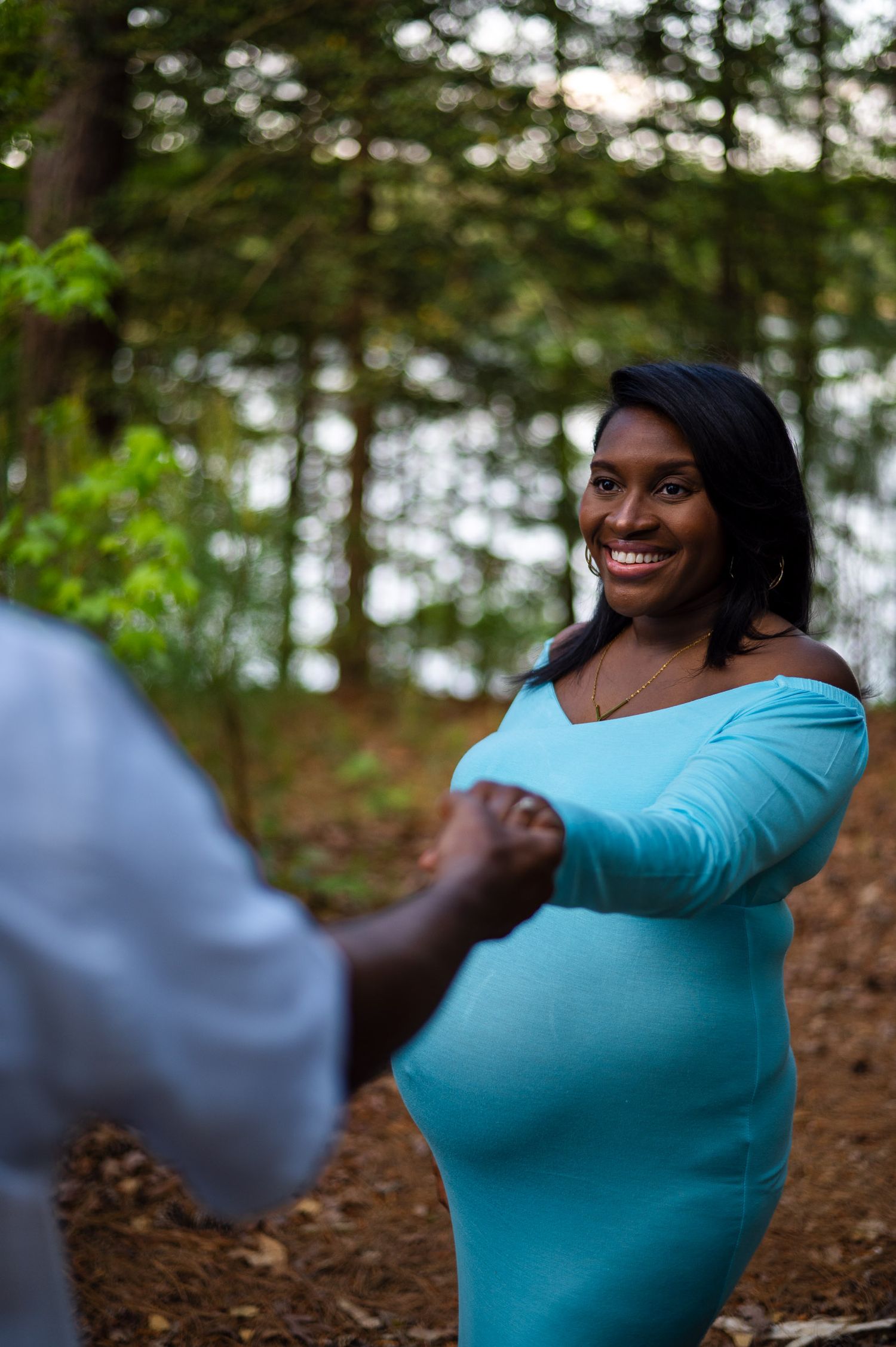 Someone wearing a turquoise dress holds hands with another person during a photo session in a wooded outdoor setting.