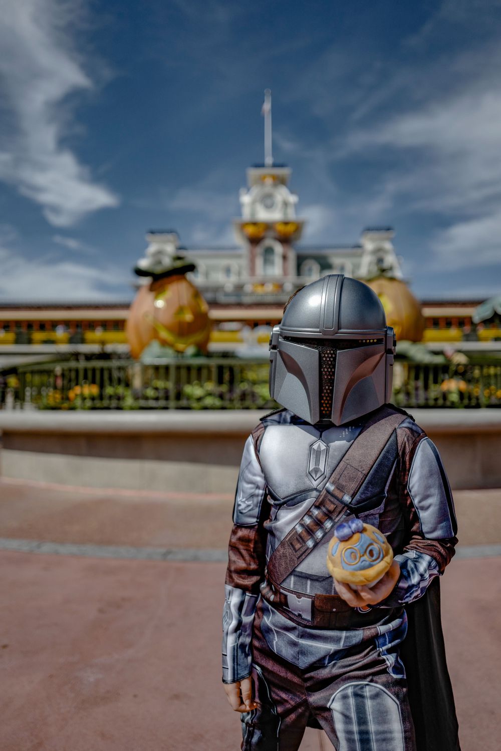 The Mandalorian costume character poses in front of Magic Kingdom entrance with golden pumpkins.