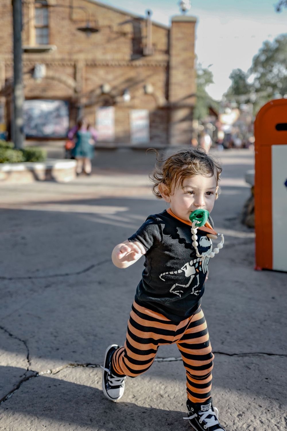 A child in striped pants and a black shirt runs playfully on a sidewalk.
