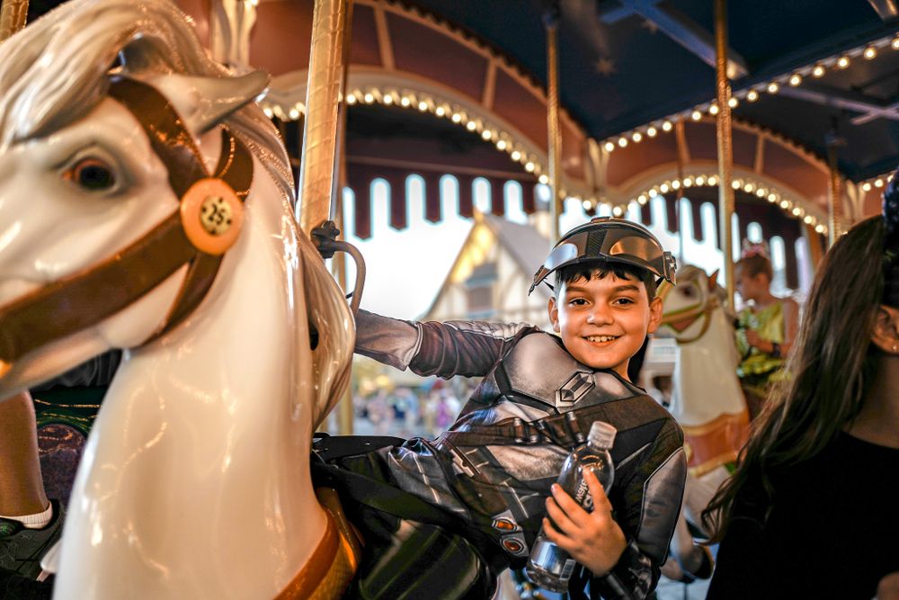 A carousel horse and rider at a theme park illuminated by decorative lights.