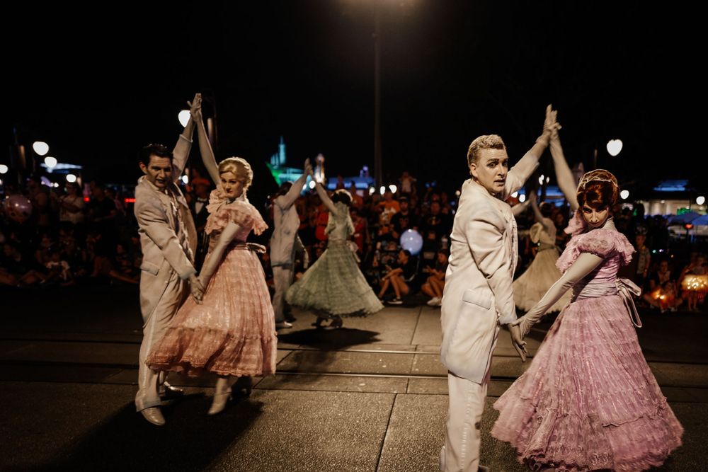 Couples dancing in vintage-style dresses and suits during a nighttime performance.