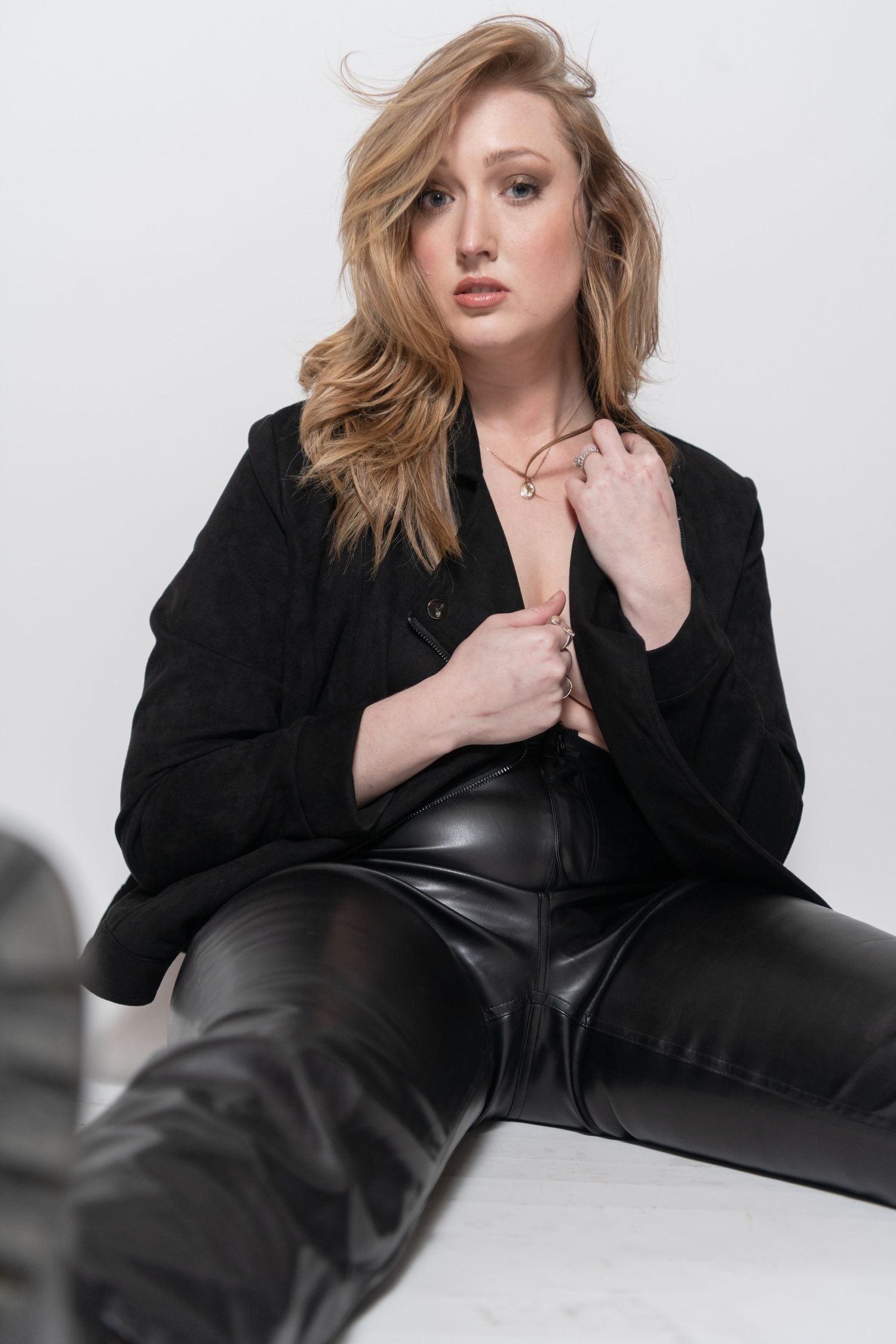 Fashion portrait in black blazer and leather pants against white backdrop.