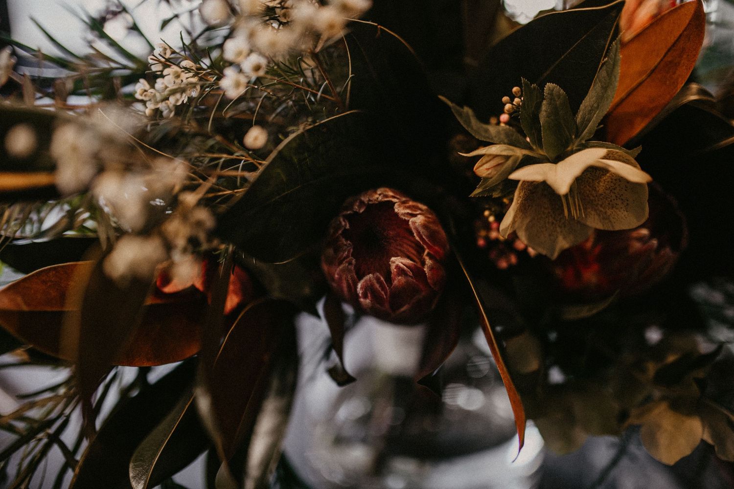 Golden autumn wedding decorations with dried flowers and orange leaves on dark rustic table settings.