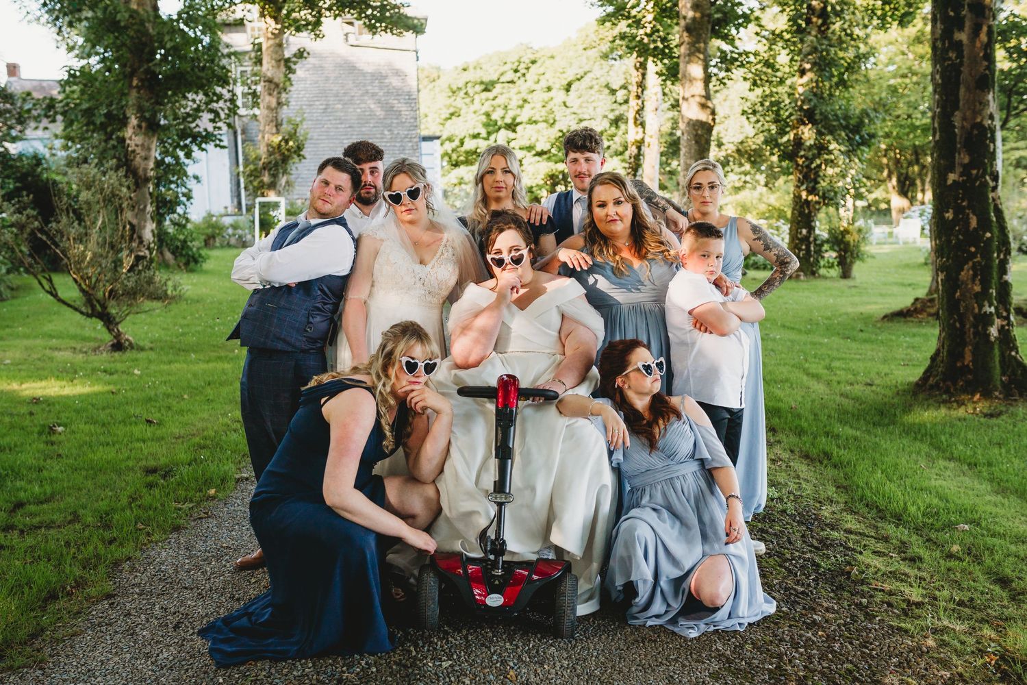 Wedding party posing for group photos in lush green garden setting.
