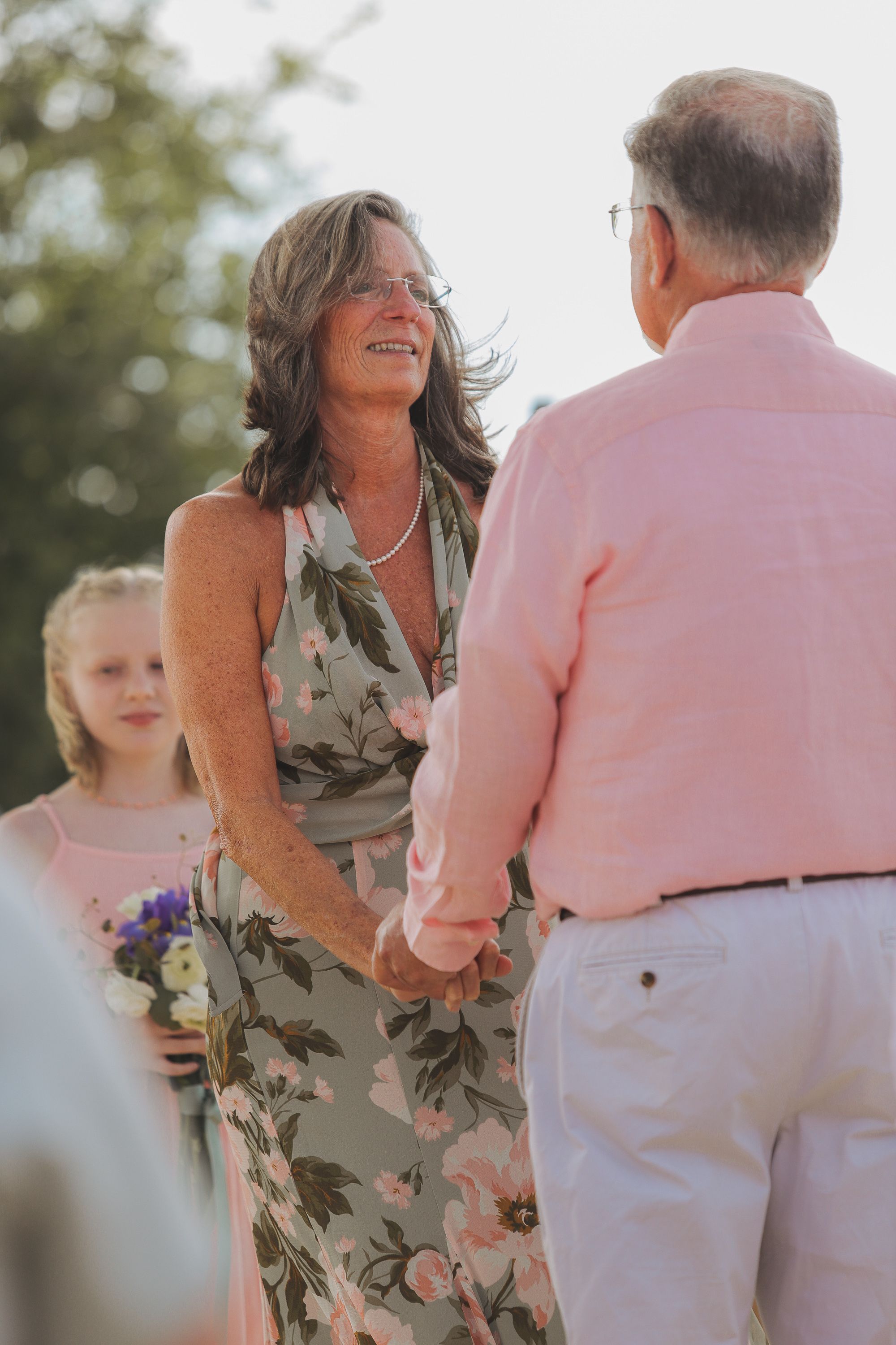 A couple shares a joyful moment during an outdoor ceremony with a child in pink in the background.