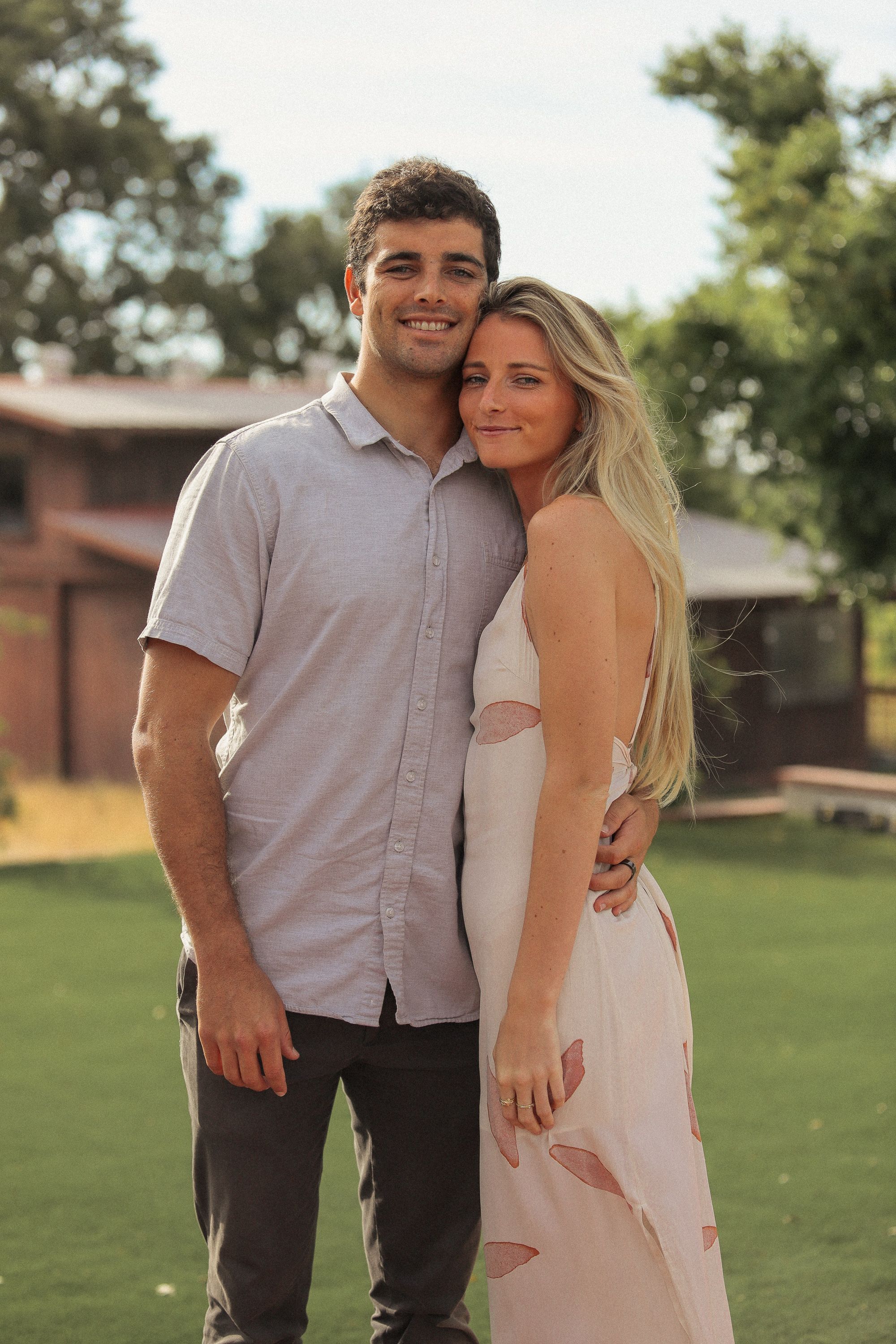 A couple in casual formal wear embracing while posing for a photo on a lawn.